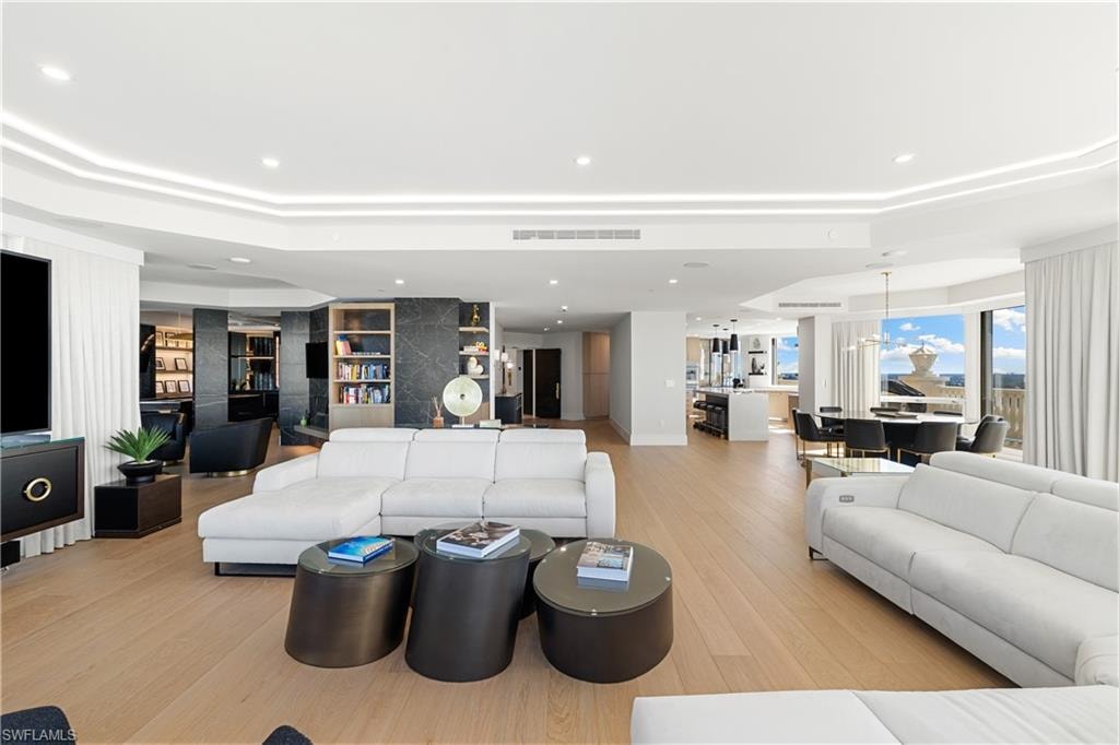 Living area featuring light wood finished floors, a tray ceiling, built in features, and recessed lighting