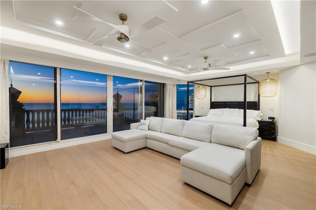 Bedroom featuring access to exterior, light wood-style flooring, a water view, recessed lighting, and a tray ceiling