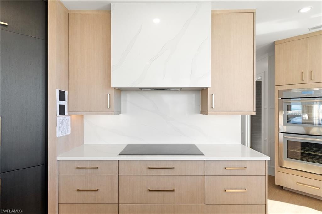 Kitchen featuring light wood finish cabinetry, stainless steel double oven, extractor fan, modern cabinets, and recessed lighting