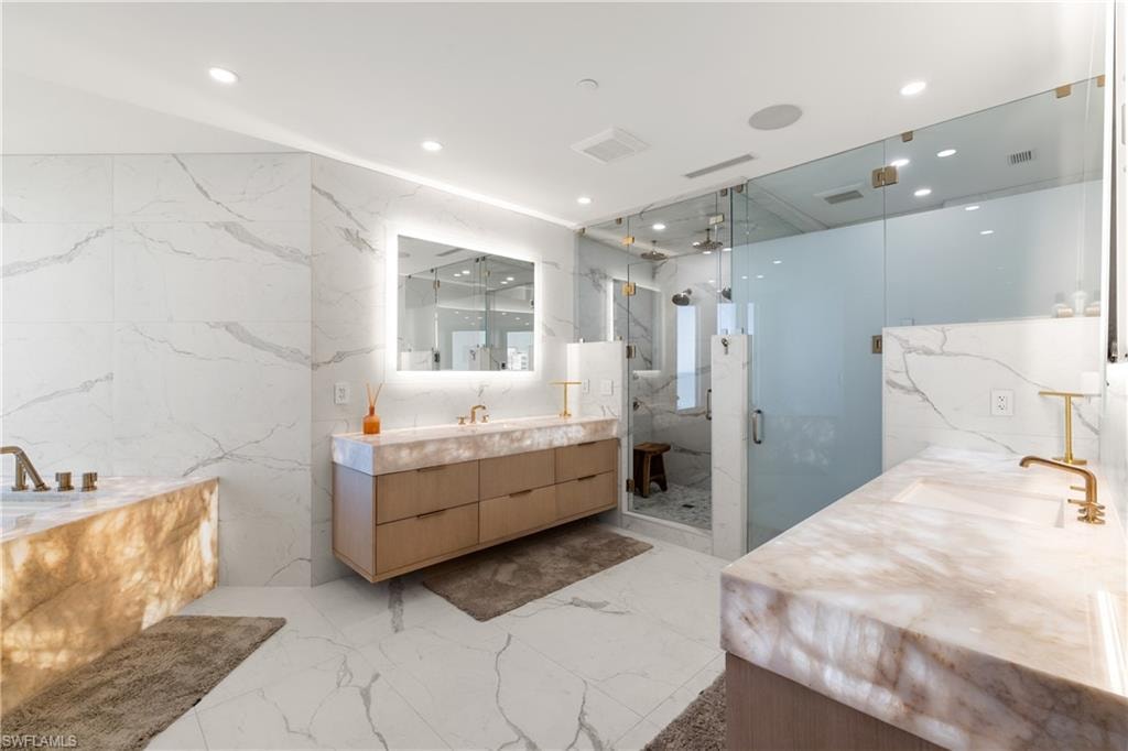 Full bathroom with stone wall, a marble finish shower, recessed lighting, tile walls, and vanity