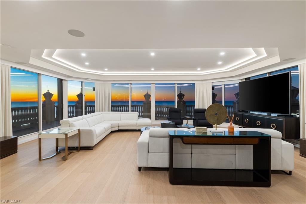 Living room featuring light wood finished floors, a tray ceiling, a water view, and recessed lighting