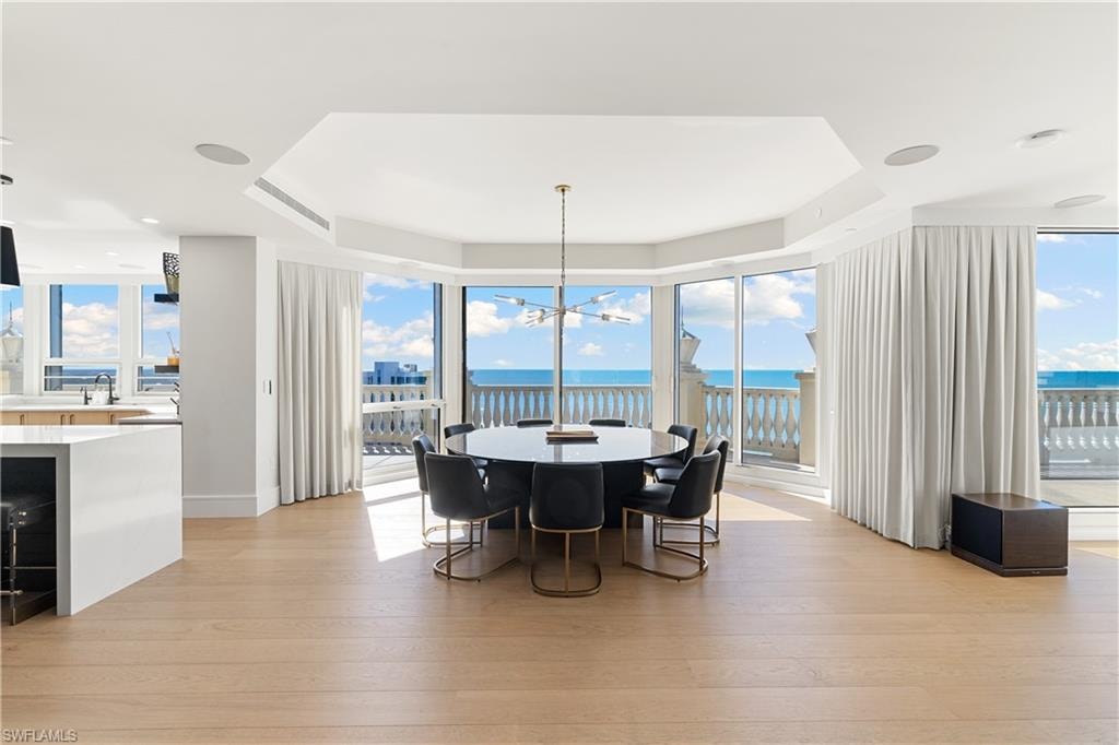 Dining area with a tray ceiling, light wood-type flooring, a water view, and hanging lights
