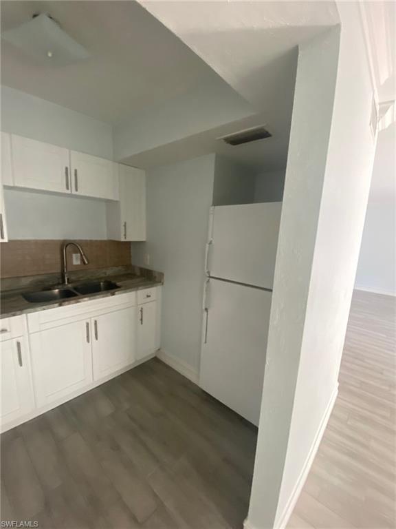 Kitchen with freestanding refrigerator, dark countertops, white cabinets, and dark wood finished floors