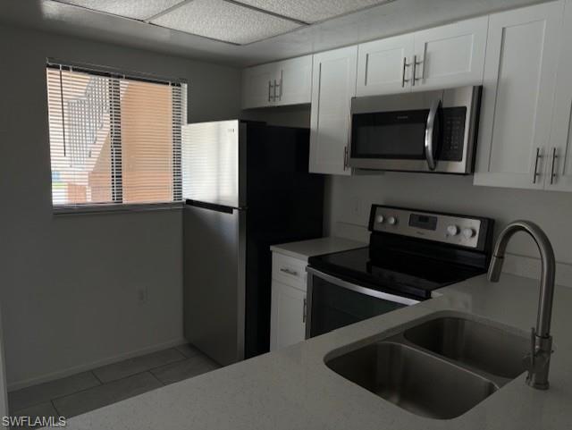 Kitchen with stainless steel appliances, light tile patterned floors, light countertops, and white cabinetry