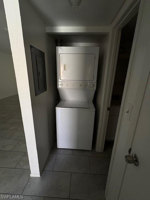 Laundry area featuring stacked washer / drying machine, electric panel, and light tile patterned flooring