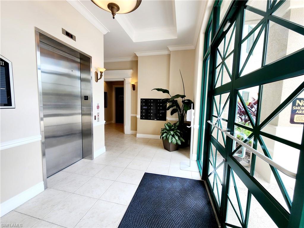 Foyer featuring elevator, mail area, a raised ceiling, light tile patterned flooring, and ornamental molding