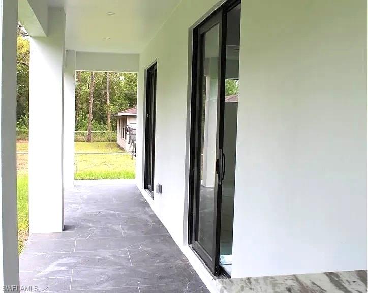 Covered patio featuring rectangular floor tiles in a dark finish, white columns, a white ceiling with recessed lighting, and black-framed sliding glass doors