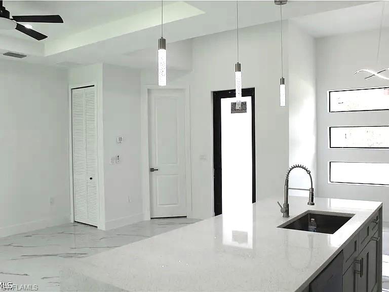 Kitchen island featuring a single basin sink with a gooseneck pull-down faucet, light-toned countertop, and dark cabinetry