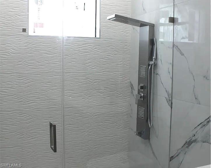 Shower enclosure featuring a multi-function shower panel with a rainfall head and hand sprayer, white wave-patterned wall tiles, and large format marbled wall tiles