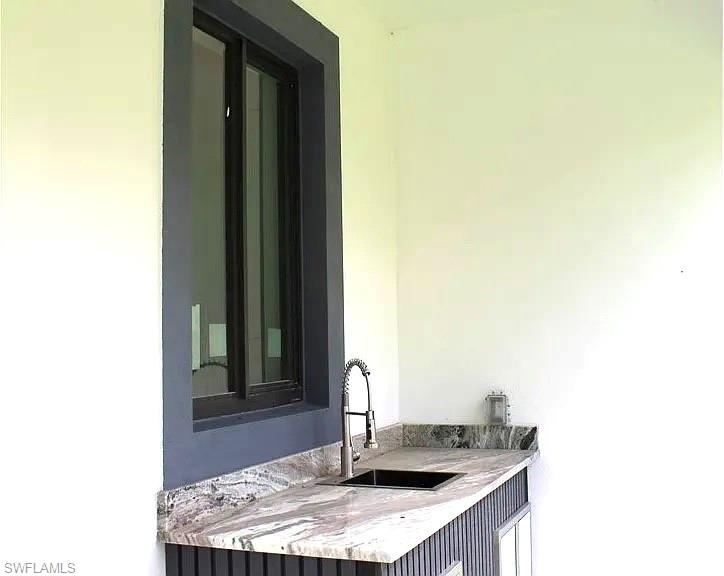 Outdoor kitchen area featuring a dark framed window, a stone countertop with natural veining, a single basin sink, and a gooseneck faucet