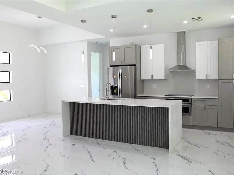 Contemporary kitchen featuring an oversized island with a waterfall countertop and slat panel detailing, stainless steel appliances, and two-tone cabinetry
