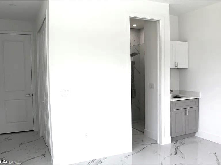 Contemporary interior featuring white walls, large format tile flooring with dark veining, a built-in vanity with grey cabinetry, a white upper cabinet, and a shower enclosure with tiled walls