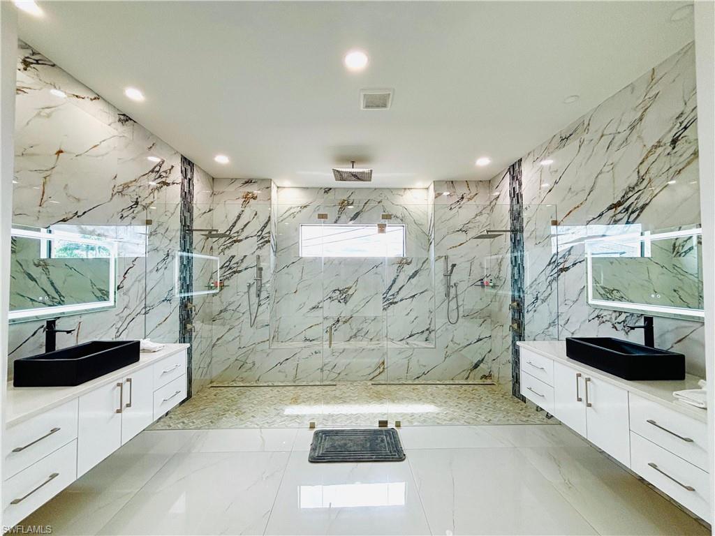 Bathroom with a marble finish shower, tile walls, two vanities, recessed lighting, and stone wall