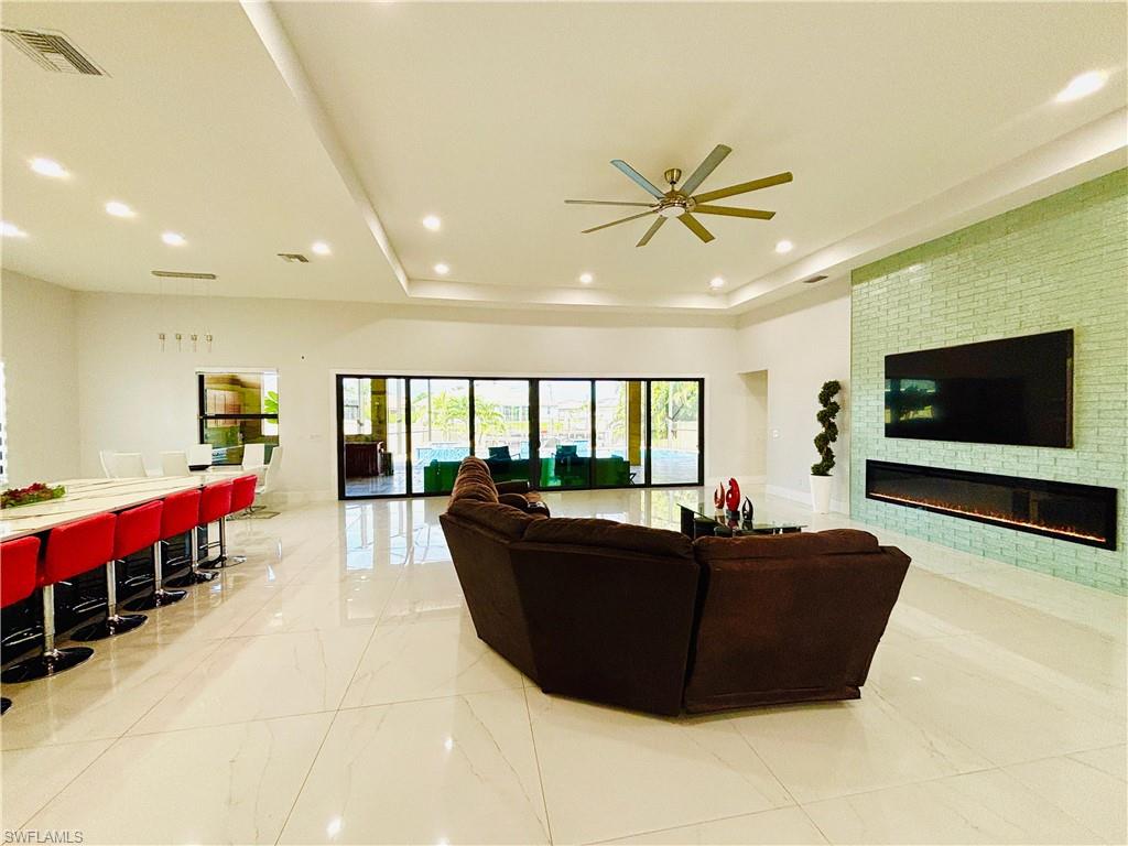 Living area with a ceiling fan, a glass covered fireplace, a raised ceiling, and recessed lighting