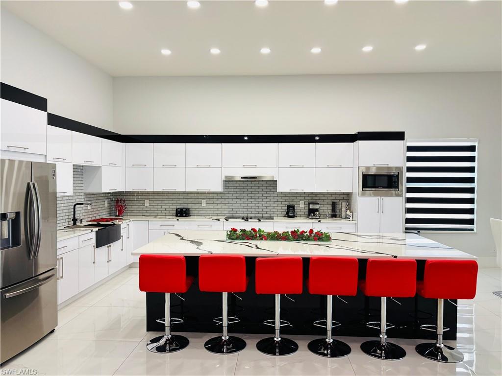 Kitchen featuring stainless steel appliances, a spacious island, modern cabinets, light stone countertops, and two tone color scheme