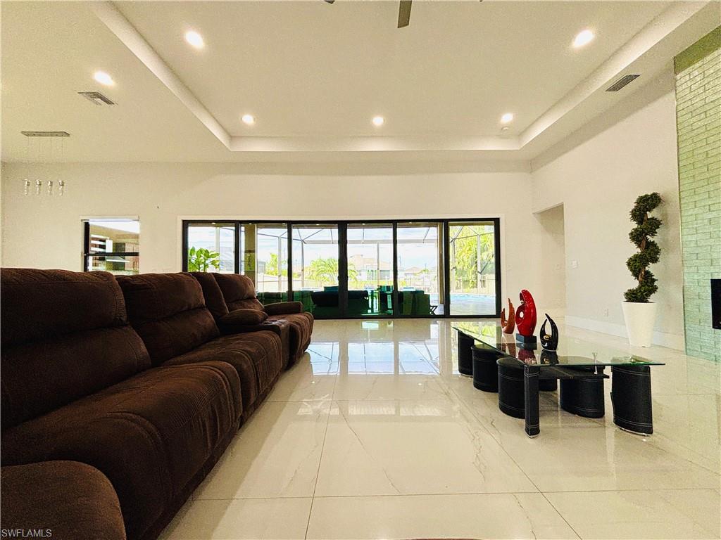 Living room featuring a tray ceiling, a ceiling fan, light marble finish flooring, and recessed lighting