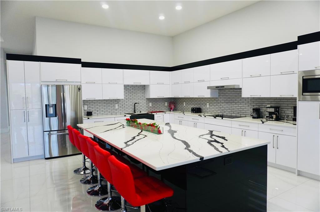 Two tone kitchen with stainless steel appliances, a center island, modern cabinets, light stone counters, and a kitchen bar