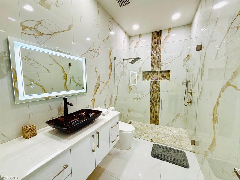 Full bath featuring vanity, a marble finish shower, and stone wall