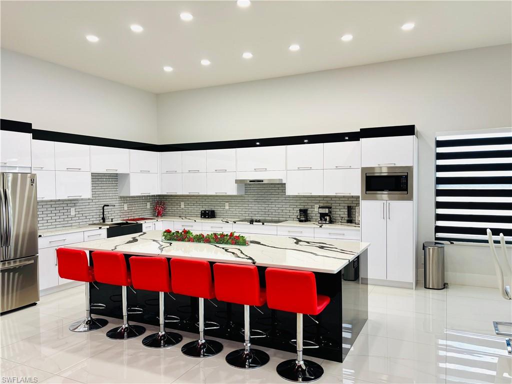 Dual tone kitchen with stainless steel appliances, a kitchen bar, light stone counters, modern cabinets, and a spacious island