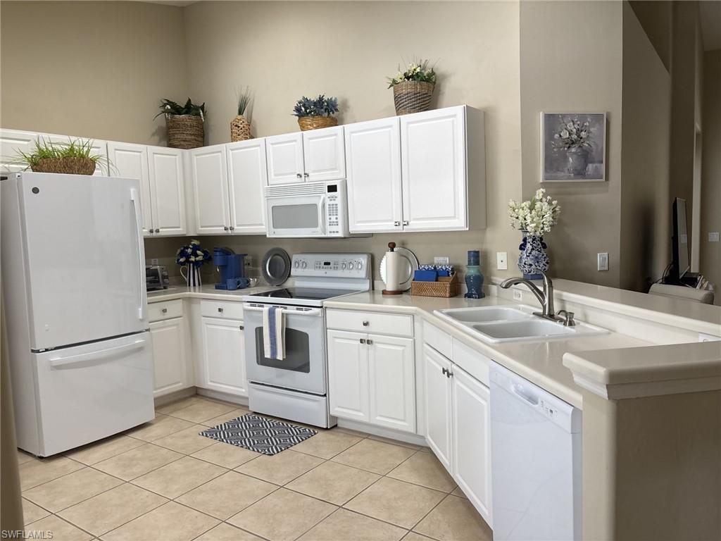 Kitchen with white appliances, white cabinets, a peninsula, and light countertops