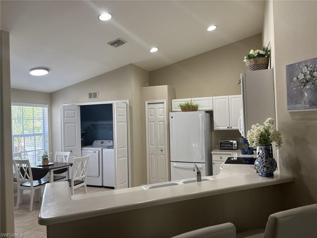 Kitchen featuring white cabinetry, light countertops, vaulted ceiling, freestanding refrigerator, and separate washer and dryer