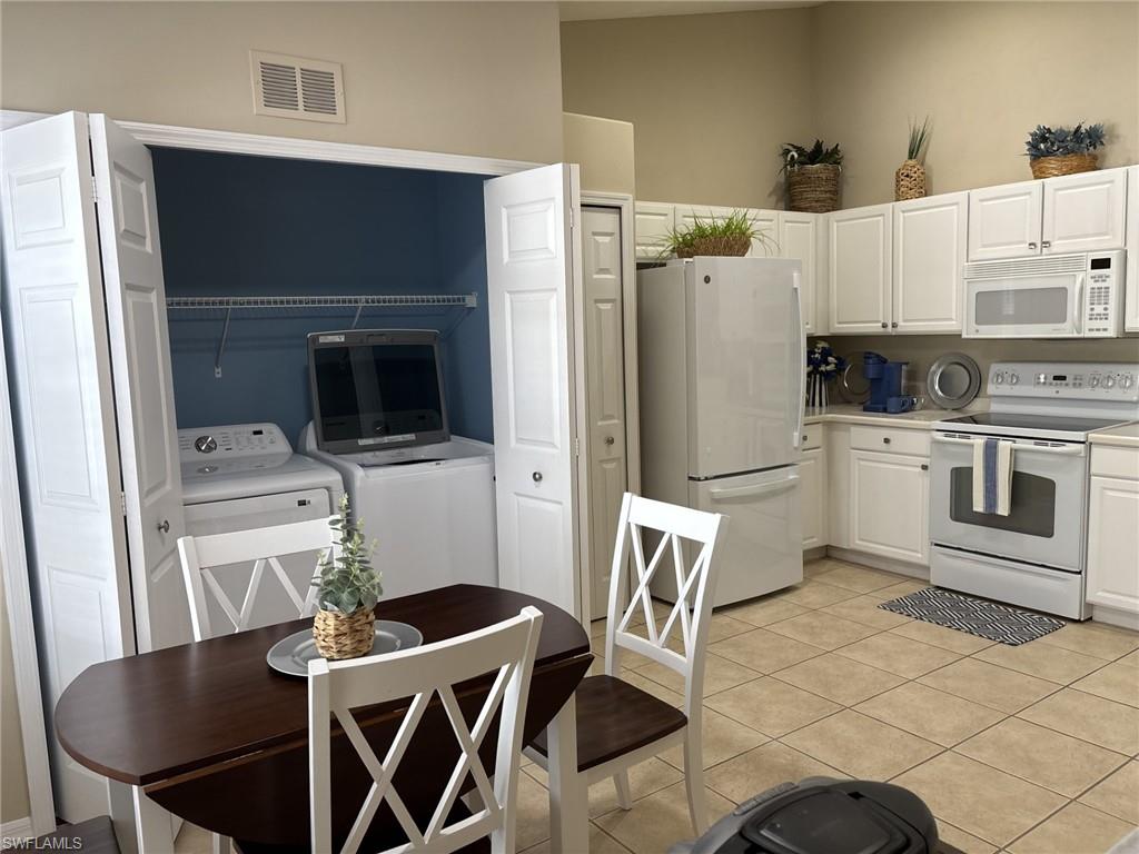 Kitchen featuring white appliances, white cabinetry, light countertops, independent washer and dryer, and light tile patterned flooring