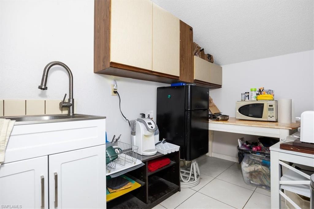 Kitchen featuring freestanding refrigerator, white microwave, light tile patterned floors, and a textured ceiling