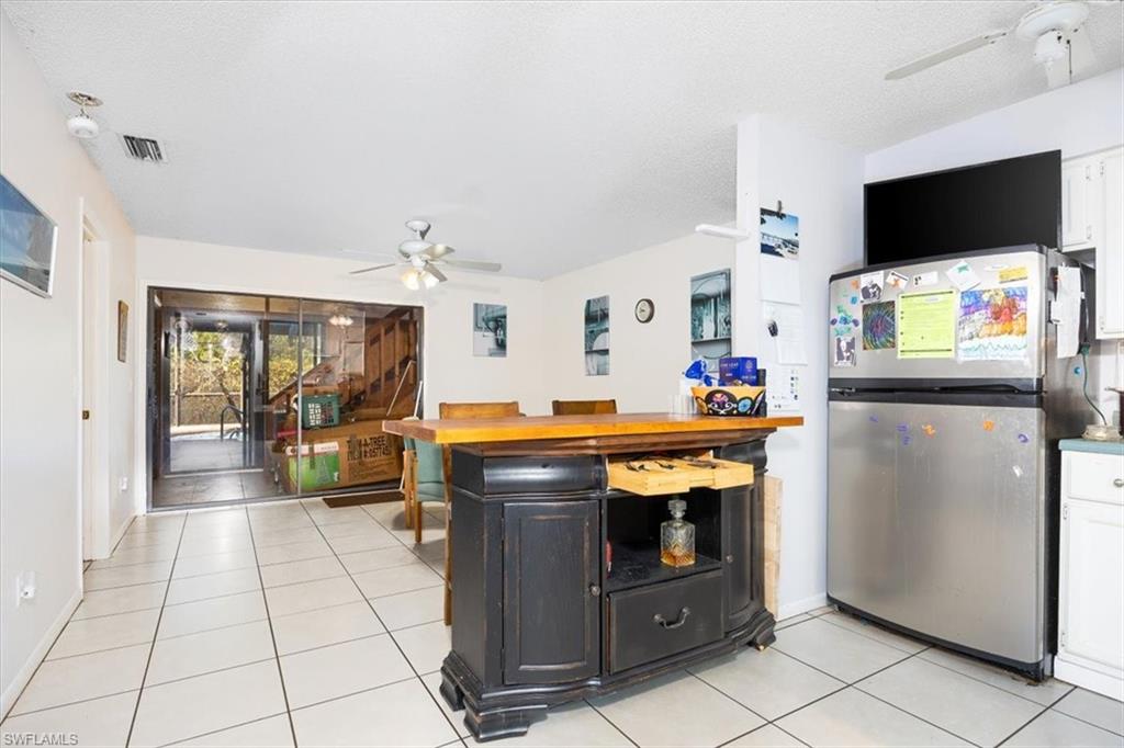 Kitchen with ceiling fan, freestanding refrigerator, light tile patterned floors, butcher block countertops, and a textured ceiling