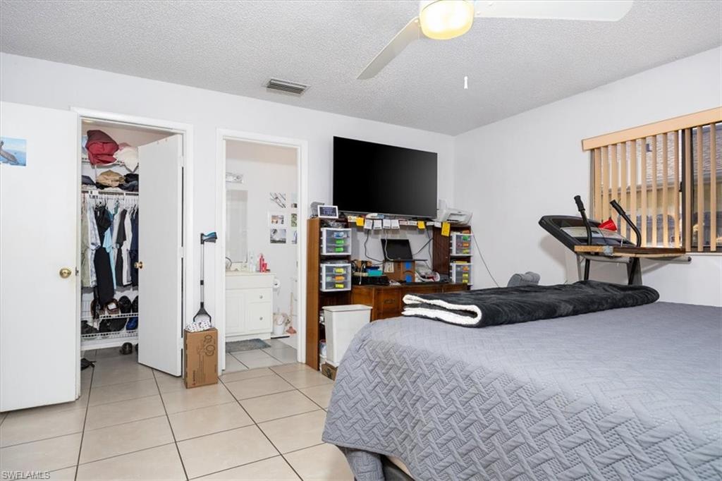 Bedroom with a textured ceiling, a spacious closet, light tile patterned flooring, and ceiling fan