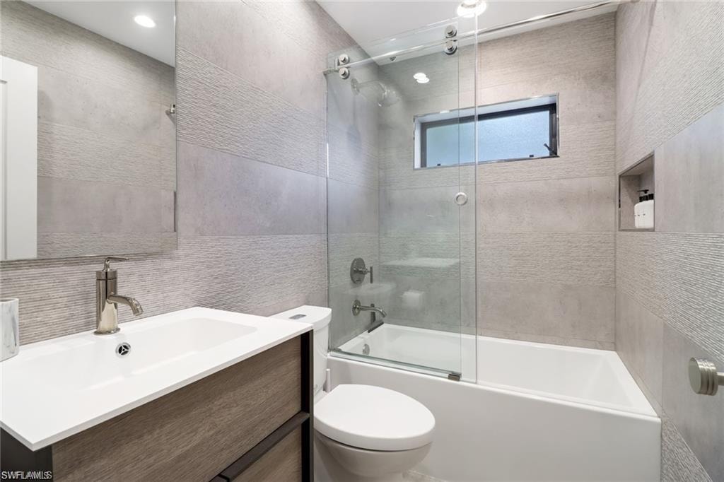 Full bathroom featuring tile walls, shower / bath combination with glass door, vanity, and toilet