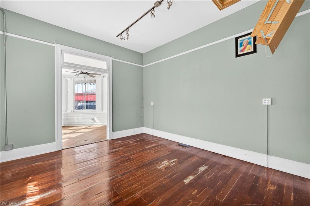 Empty room with dark wood finished floors, rail lighting, and a ceiling fan