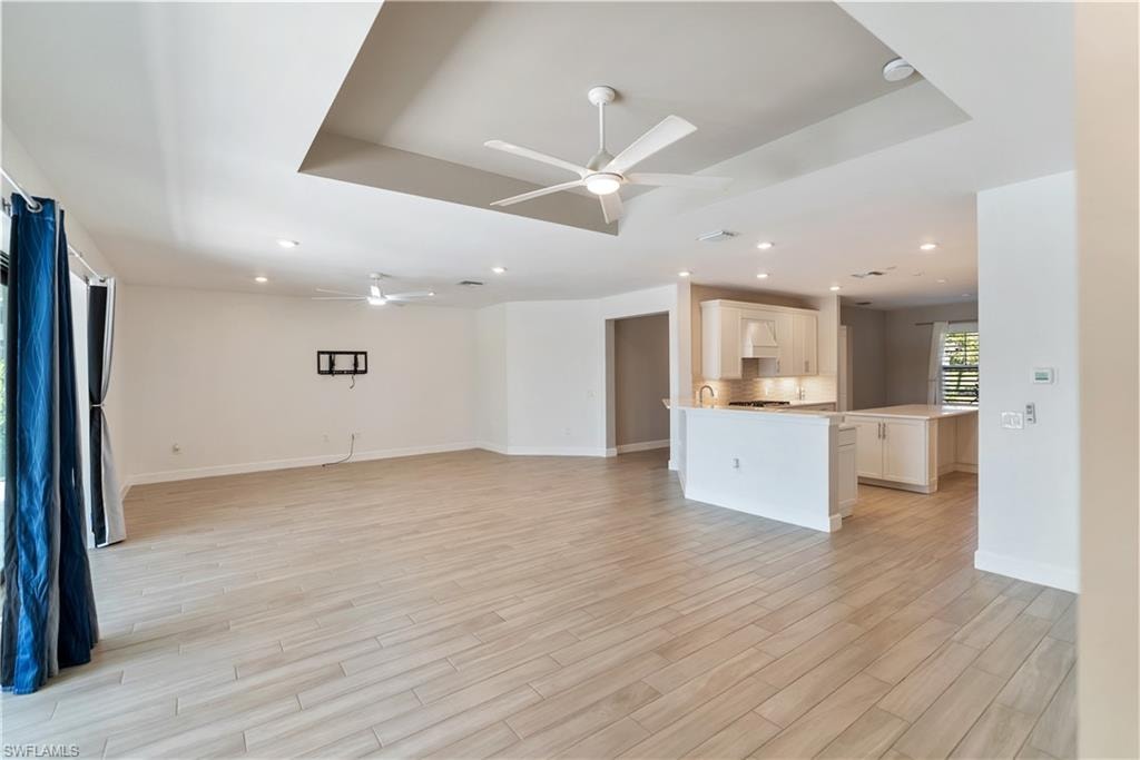 Unfurnished living room featuring 2 ceiling fans, a raised ceiling, light wood-type tile flooring, and recessed lighting