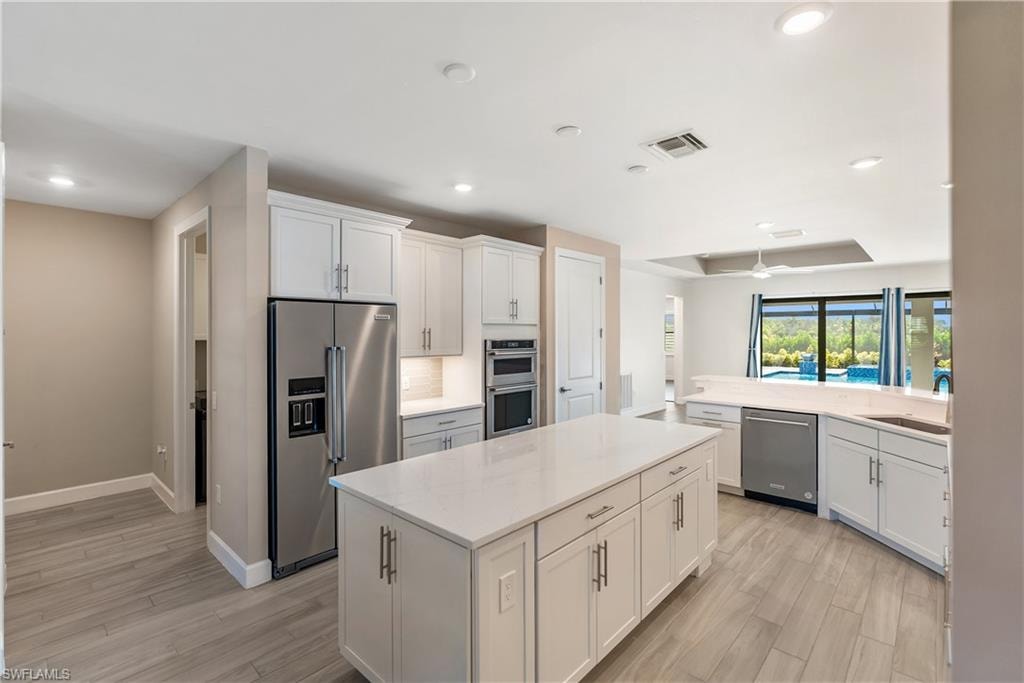 Kitchen with stainless steel appliances, white cabinetry, a center island, light wood-style flooring, and recessed lighting