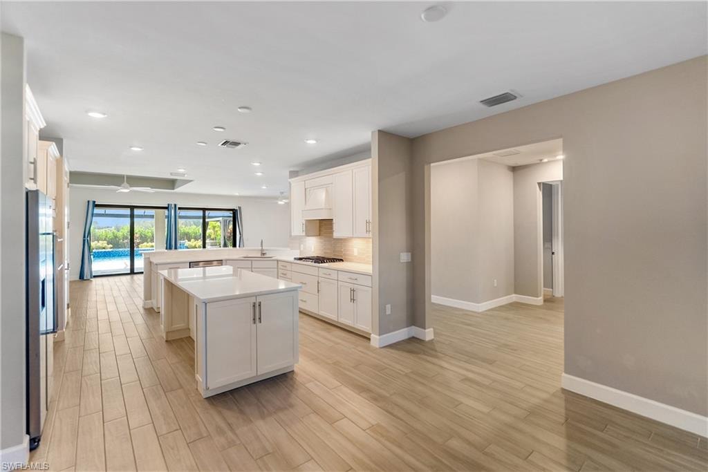 Kitchen with a peninsula, a center island, light wood finished tile floors, white cabinetry, and stainless steel appliances