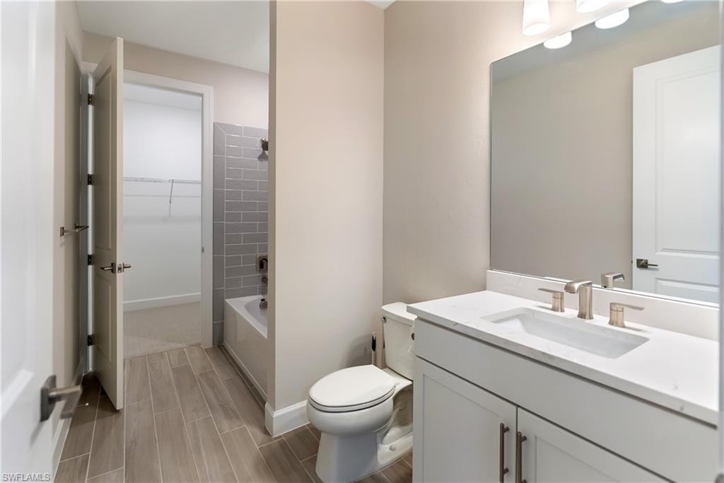 Ensuite bathroom with vanity, shower / bath combination, wood finish floors, and a walk in closet