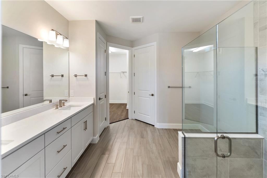Primary bathroom featuring a walk in closet, double vanity, light wood-style floors, and a stall shower