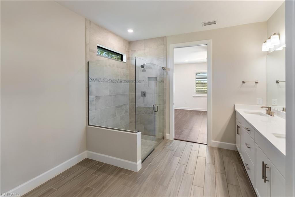 Primary bath with healthy amount of natural light, a stall shower, wood finish floors, and recessed lighting
