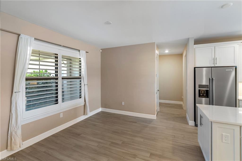 Kitchen with white cabinets, light wood-type tile flooring, stainless steel fridge with ice dispenser, light stone countertops, and recessed lighting