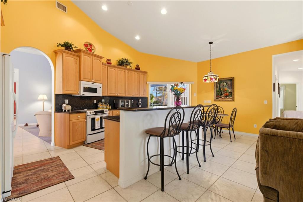 Kitchen with arched walkways, a breakfast bar, white appliances, and light tile patterned floors