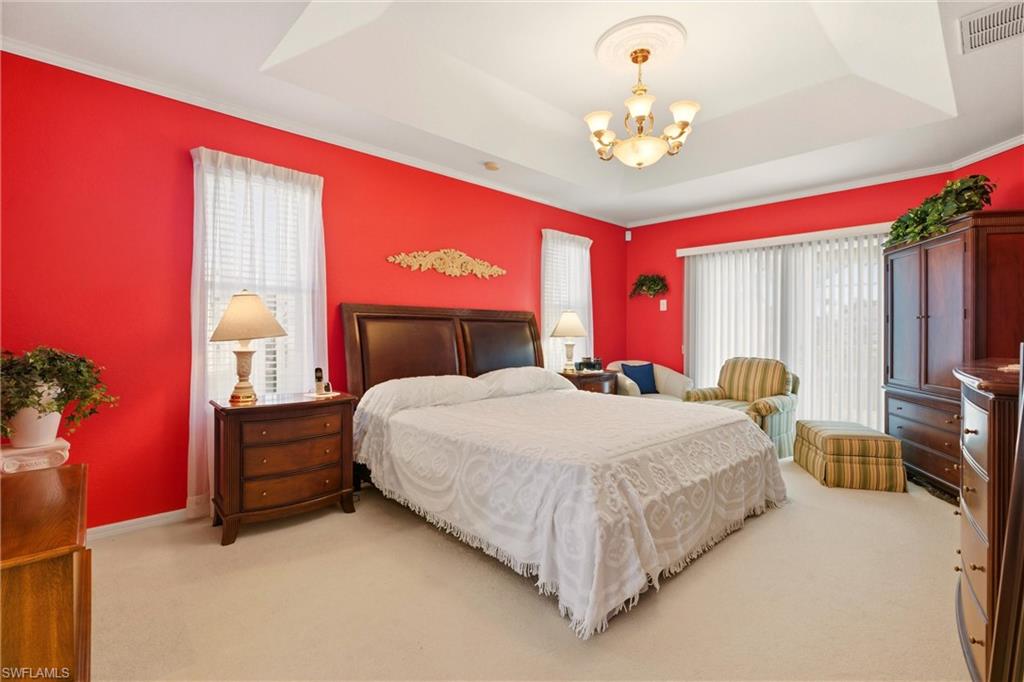 Bedroom featuring light carpet, multiple windows, hanging lights, and ornamental molding