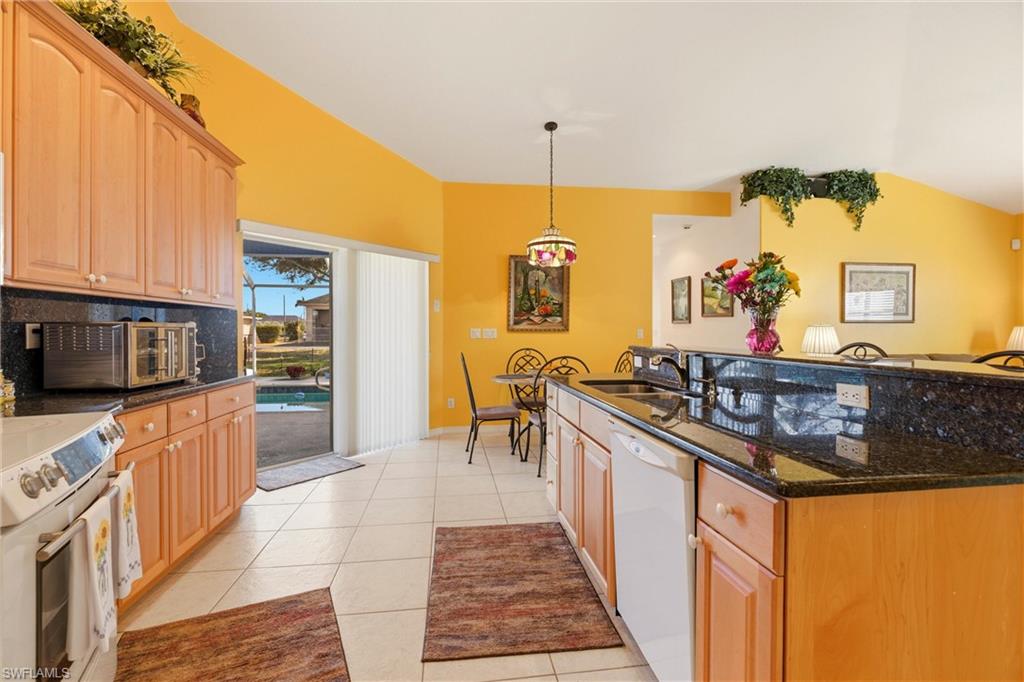 Kitchen featuring dark stone countertops, white appliances, hanging light fixtures, lofted ceiling, and light tile patterned floors