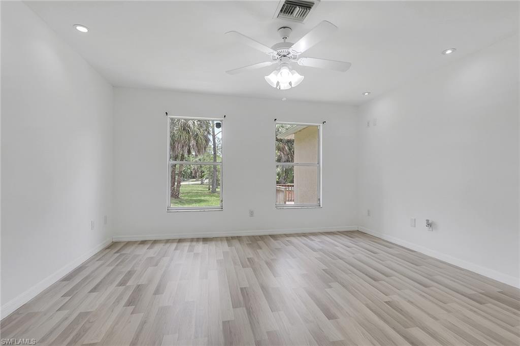 Spacious room featuring wood-finish flooring, two windows, recessed lighting, a ceiling fan with light fixture, and white painted walls
