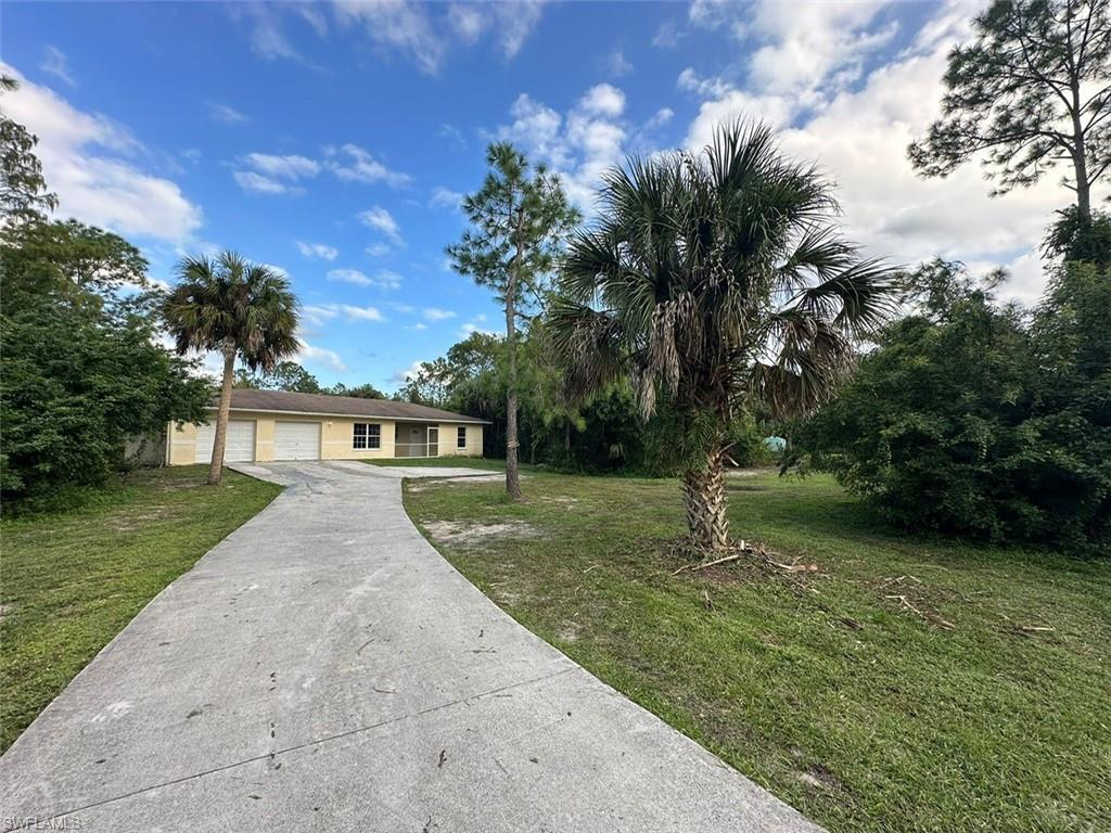 Long concrete driveway leading to a single-story residence with a light-colored exterior