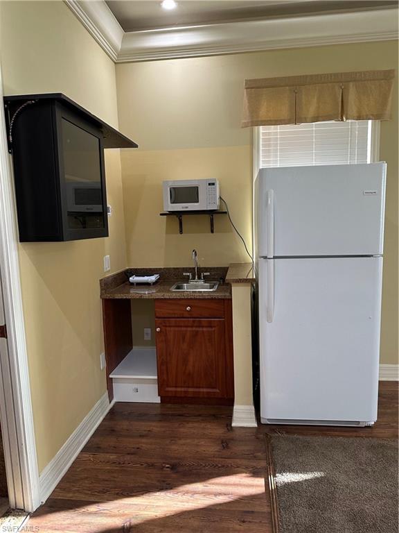 Compact kitchenette featuring a stainless steel sink, dark wood-finish cabinetry, a stone-finish countertop, and wood-finish flooring