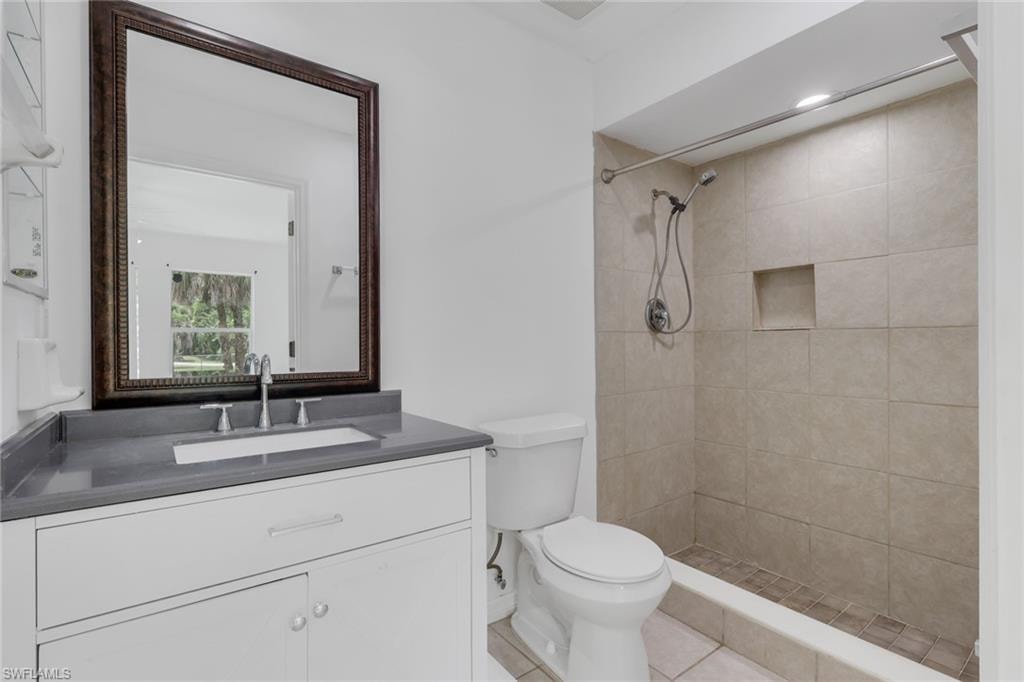 Bathroom featuring a single vanity with an integrated sink and gray countertop, a framed wall mirror, a commode, and a shower with tiled walls and a recessed niche
