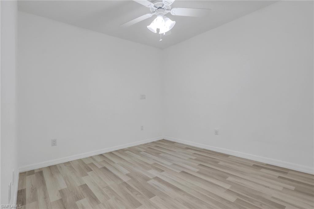 Room featuring light wood-finish flooring, white walls, white baseboards, and a white ceiling fan with integrated lighting