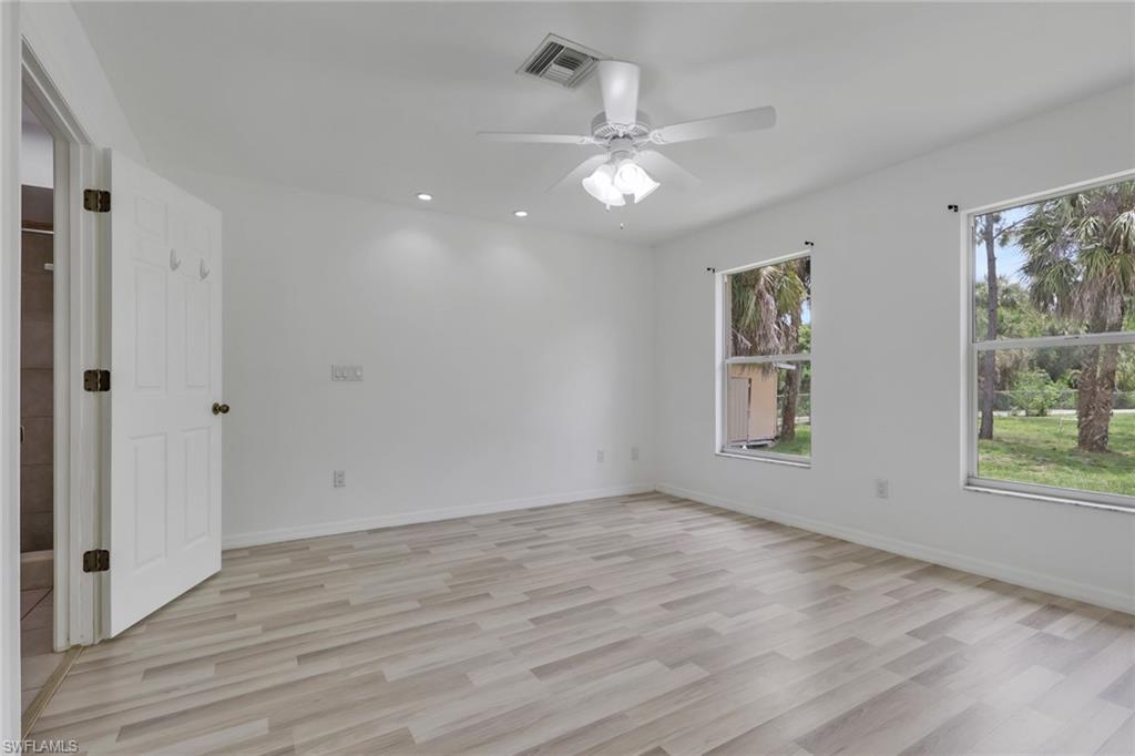 Spacious room featuring wood-finish flooring, two large windows, a ceiling fan with integrated lighting, and recessed ceiling lights
