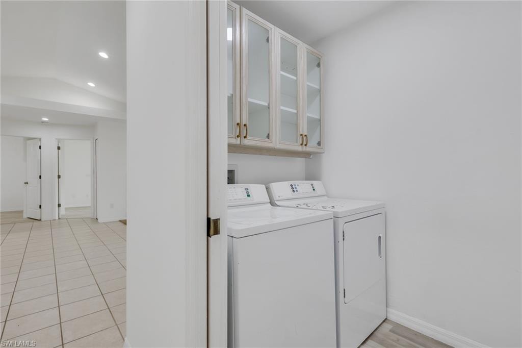 Laundry area featuring white walls, overhead cabinetry with glass inserts and brass-toned hardware, and a tile flooring