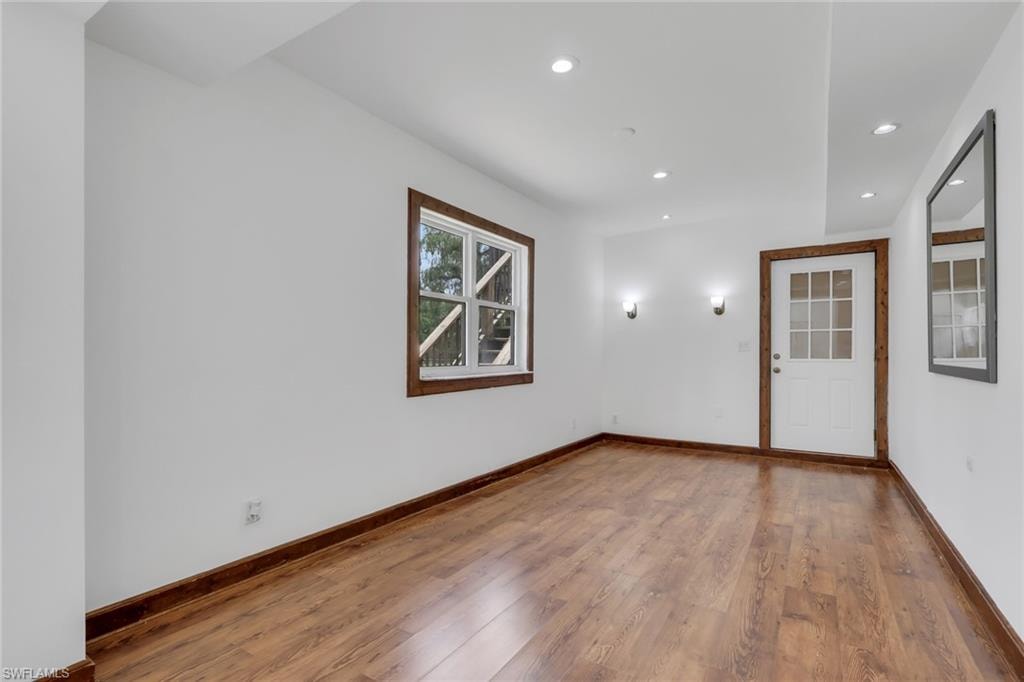 Bright interior space featuring wood-finish flooring, white walls, and a white paneled door with glass inserts