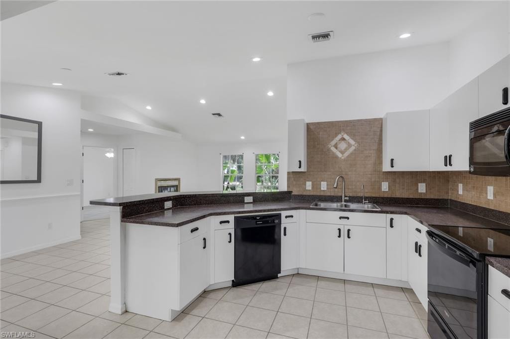 Open-concept kitchen featuring white cabinetry, dark countertops, a tiled backsplash with decorative inlay, and recessed lighting